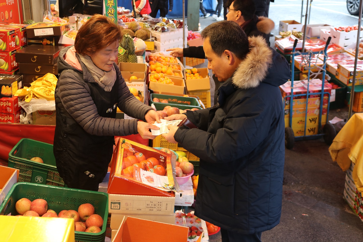 창업진흥원, 대전 중앙시장에서 새해 설맞이 사진 세번째 - 김광현 원장님이 시장 상인에게 과일을 구매한 후 온누리 상품권으로 결제하는 사진을 촬영하고 있습니다.