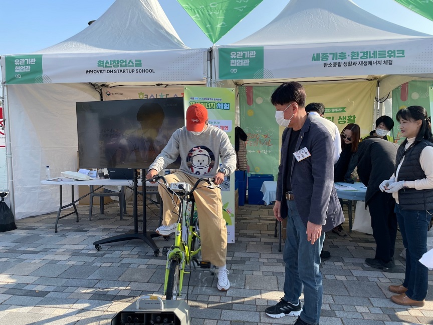 창업진흥원 원장(김용문)은 청소년비즈쿨페스티벌 참관객을 대상으로 자전거 재생에너지 발전기 체험을 지켜보는 사진 
