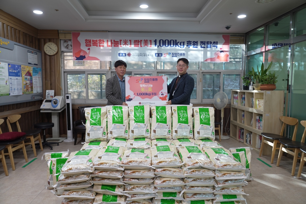 김용문 창업진흥원장과 복지관 직원이 후원되는 쌀과 함께 사진을 찍고 있음.